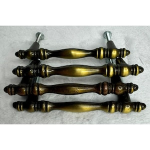 May include: Four antique brass drawer pulls with a decorative design. Each pull has a curved handle and is mounted on a metal base with screws. The pulls have a vintage, aged appearance.
