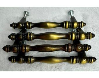 May include: Four antique brass drawer pulls with a decorative design. Each pull has a curved handle and is mounted on a metal base with screws. The pulls have a vintage, aged appearance.