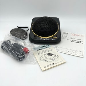 May include: A black car speaker with a gold trim and a black mesh grille. The speaker is labeled "Windy-Kid's". The speaker is accompanied by a black power cord, a black and red car charger, and a black and white instruction manual.