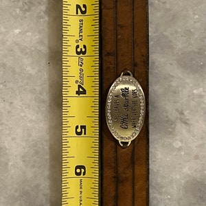 May include: A brown leather bracelet with a silver charm that reads "She leaves a little sparkle wherever she goes". The charm is decorated with small rhinestones. The bracelet is 7 inches long.