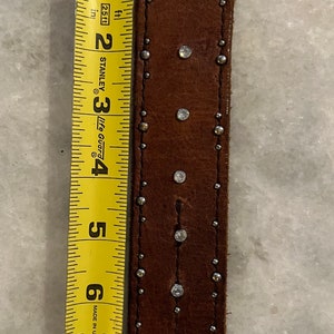 May include: Brown leather bracelet with silver studs and rhinestones. The bracelet is approximately 7 inches long.