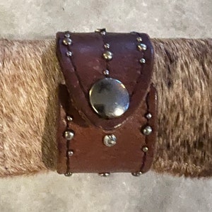 May include: A brown leather bracelet with silver studs and a silver button closure.