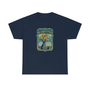 May include: A navy blue t-shirt with a vintage-style graphic of a person with a snake wrapped around their head. The graphic is surrounded by a yellow frame with the text "BIG SOMETHING" in yellow letters.
