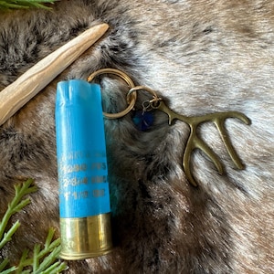 May include: A blue shotgun shell keychain with a gold antler charm and a blue crystal. The keychain is on a brown faux fur background.