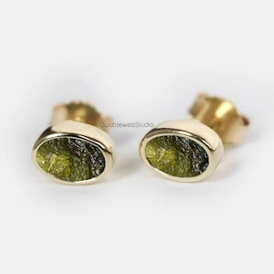 May include: A pair of gold earrings with oval-shaped green stones. The stones have a unique, textured appearance.