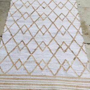 May include: White and tan diamond patterned rug. The rug features a repeating diamond design in tan against a white background. The bottom edge has horizontal tan stripes and fringe.