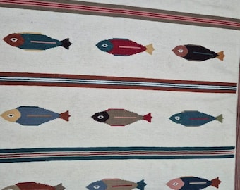 May include: A rectangular, off-white rug with a repeating pattern of colorful fish. The fish are in shades of blue, brown, red, and green, with red or yellow fins. The rug has horizontal stripes in blue, brown, and red.