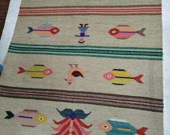 May include: Beige woven rug with colorful fish and whimsical figures. The rug features horizontal stripes in various colors, including red, blue, and brown. The fish are in shades of red, pink, yellow, and blue. A decorative floor covering.