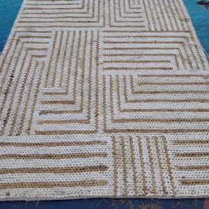 May include: A white and brown woven rug with a geometric pattern. The rug has a rectangular shape and is made of natural fibers.