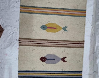 May include: Rectangular beige rug with a repeating fish pattern. Each fish is a different color, including red, yellow, purple, and teal. The rug also features horizontal stripes in various colors.