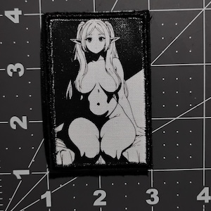 May include: Black and white embroidered patch featuring an anime-style female character with pointed ears. The character is depicted in a seated pose with long hair and a bow tie. The patch has a rectangular shape with a black border.