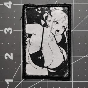 May include: Black and white patch featuring an anime-style illustration of a female character. The character has large eyes, pointed ears, and is wearing a bikini top with heart-shaped accents. The patch has a black border.