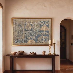 May include: A framed artwork with a gold frame hangs above a dark wood table. The artwork features a blue background with gold-colored illustrations. Two brass candle holders and decorative bowls are on the table.