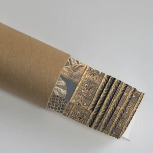 May include: A rolled-up brown cardboard tube with a stack of patterned prints. The prints feature a repeating design in shades of brown, gold, and gray. The prints are partially visible, showcasing the intricate patterns.