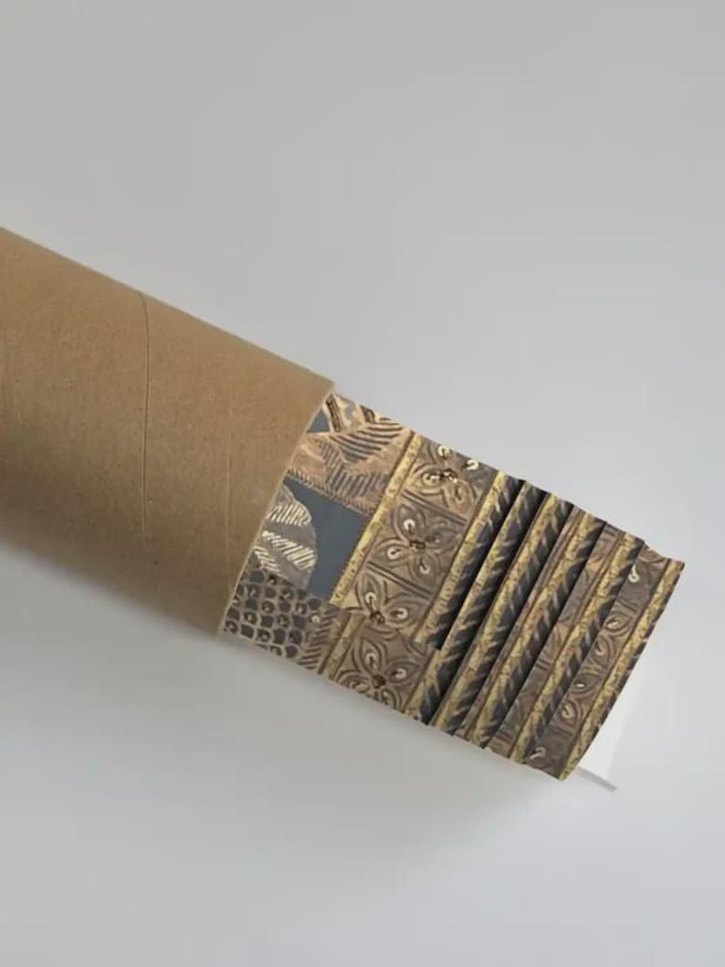 May include: A rolled-up brown cardboard tube with a stack of patterned prints. The prints feature a repeating design in shades of brown, gold, and gray. The prints are partially visible, showcasing the intricate patterns.
