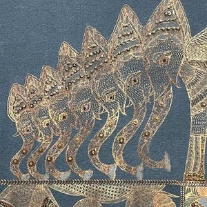 May include: A detailed textile featuring a row of elephants with ornate, embellished designs in gold and silver thread. The elephants are arranged in a line, with their trunks curved. Below the elephants are fish. The background is a muted teal color.
