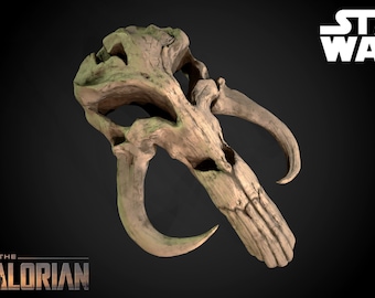 May include: A beige and green Mandalorian skull prop from the Star Wars series. The skull has two large horns and a detailed design.