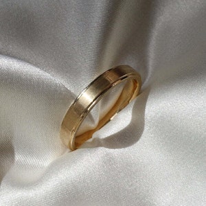May include: A simple gold wedding band with a slightly rounded edge.
