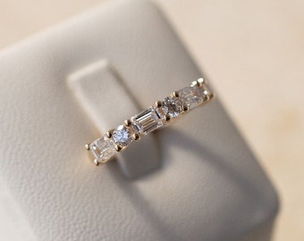 May include: A gold band ring with a row of clear, rectangular-shaped diamonds set in a prong setting.