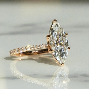 May include: A rose gold engagement ring with a large marquise-shaped diamond and a diamond-encrusted band.
