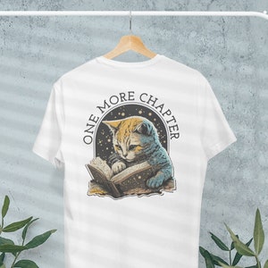 May include: White t-shirt with a graphic of a cat reading a book with stars in the background. The text "One More Chapter" is printed in a circle around the cat.