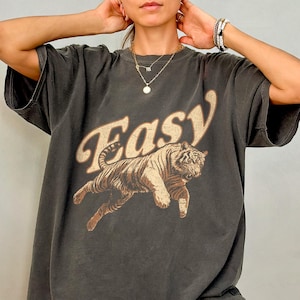 Peut inclure: Un t-shirt surdimensionn&eacute; gris fonc&eacute; avec un motif de tigre et le mot "Easy" imprim&eacute; sur le devant.