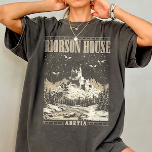 Könnte beinhalten: Ein schwarzes Oversize-T-Shirt mit einem grafischen Druck eines Schlosses, Drachen und Sternen. Der Text "RIORSON HOUSE" und "ARETIA" ist auf dem Shirt gedruckt.