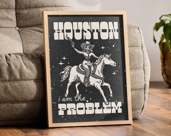 Könnte beinhalten: Ein gerahmter Druck mit schwarzem Hintergrund, der eine Frau auf einem Pferd zeigt. Die Frau trägt einen Cowboyhut und hält eine Pistole. Der Text "HOUSTON I AM THE PROBLEM" ist in Weiß auf dem Druck gedruckt.