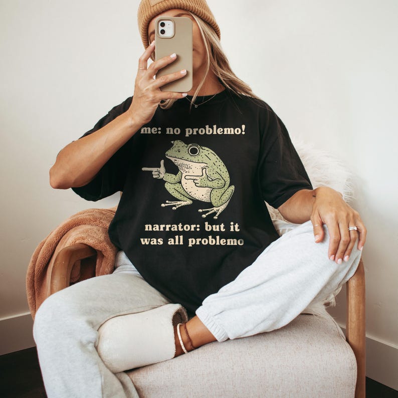 May include: Black t-shirt with a green frog graphic and the text "me: no problemo!" and "narrator: but it was all problemo". The frog is pointing with its finger. The shirt is a casual style.