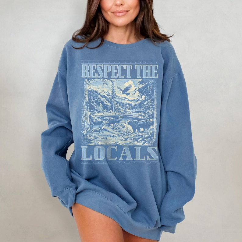 May include: A blue sweatshirt with a vintage-style graphic print of a mountain scene with the text "Respect the Locals".