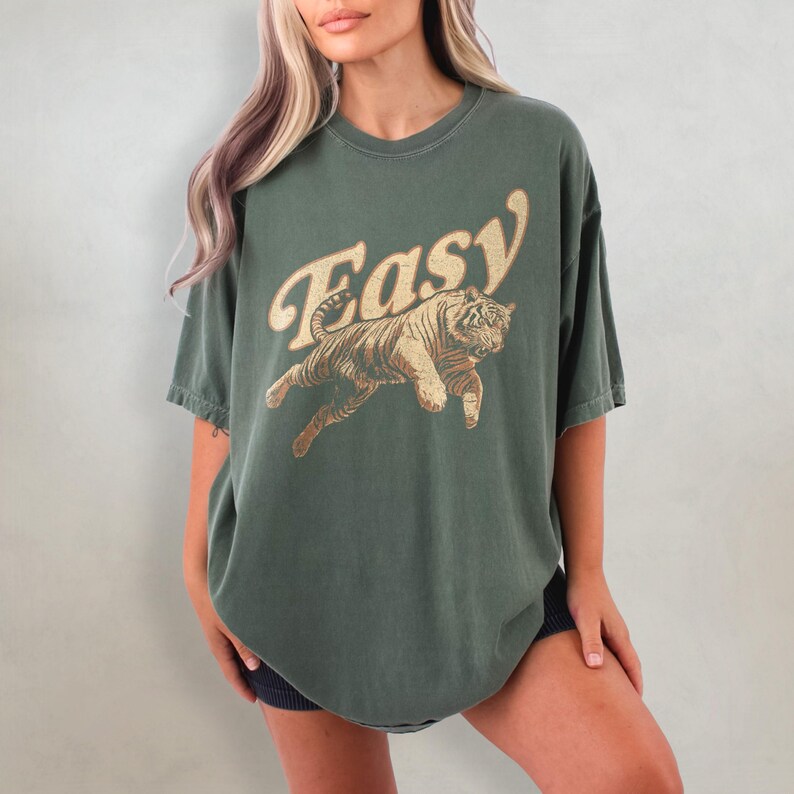 Peut inclure: Un t-shirt surdimensionn&eacute; vert avec un motif vintage d'un tigre sautant avec le mot "Easy" dans une police r&eacute;tro.