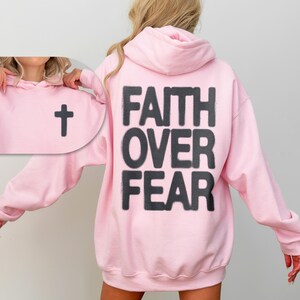 May include: Pink hooded sweatshirt with the text "FAITH OVER FEAR" printed on the back and a small cross on the front.