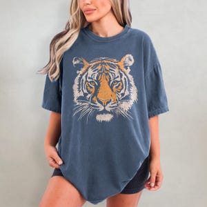 May include: A blue oversized t-shirt with a vintage-style tiger face graphic printed on the front.