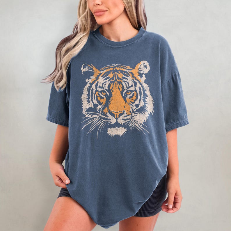 May include: A blue oversized t-shirt with a vintage-style tiger face graphic printed on the front.