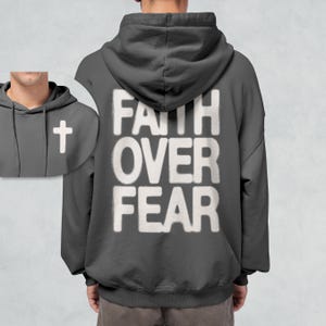 May include: A dark gray hooded sweatshirt with the phrase "FAITH OVER FEAR" printed in white on the back. A small white cross is visible on the front of the sweatshirt.