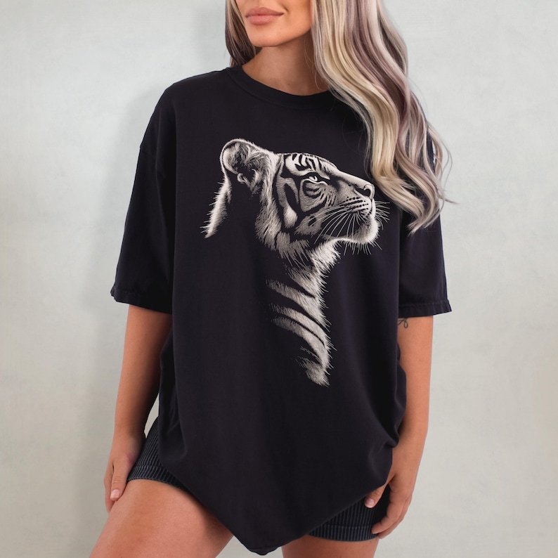 Puede incluir: Una camiseta negra de gran tama&ntilde;o con un estampado gr&aacute;fico de tigre blanco. El tigre est&aacute; mirando hacia la derecha y tiene un dise&ntilde;o detallado.