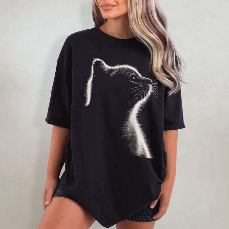 May include: Black oversized t-shirt with a white graphic of a cat's head looking to the right.