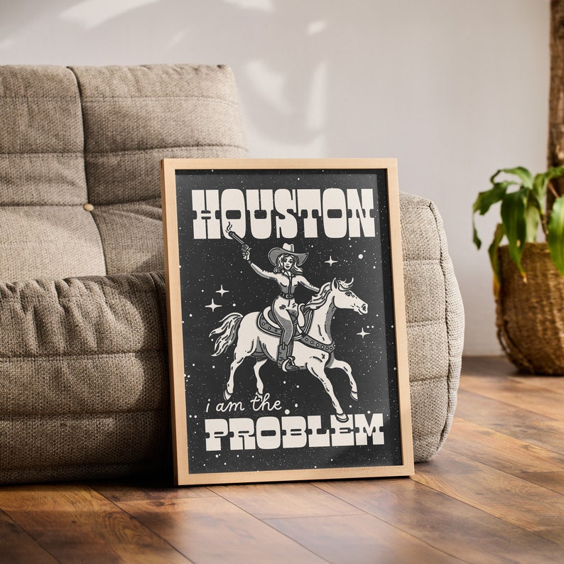 May include: A framed print with a black background featuring a woman riding a horse. The woman is wearing a cowboy hat and holding a gun. The text "HOUSTON I AM THE PROBLEM" is printed in white on the print.