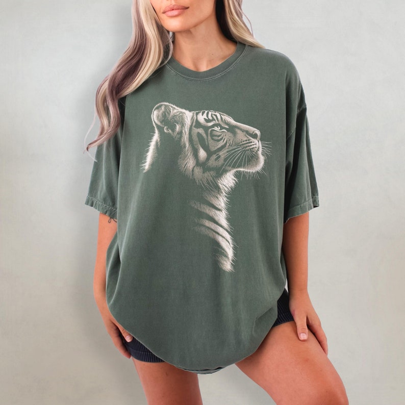 Puede incluir: Una camiseta de gran tama&ntilde;o de color verde oscuro con un gr&aacute;fico blanco de la cabeza de un tigre. El tigre est&aacute; mirando hacia la derecha.
