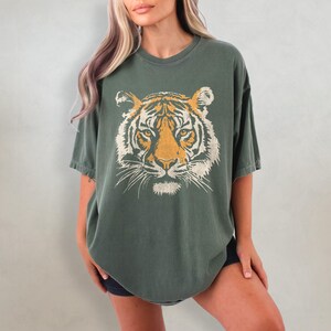 May include: A green oversized t-shirt with a vintage-style tiger face graphic printed on the front.