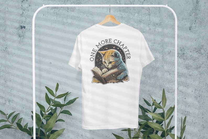 May include: White t-shirt with a graphic of a cat reading a book with stars in the background. The text "One More Chapter" is printed in a circle around the cat.
