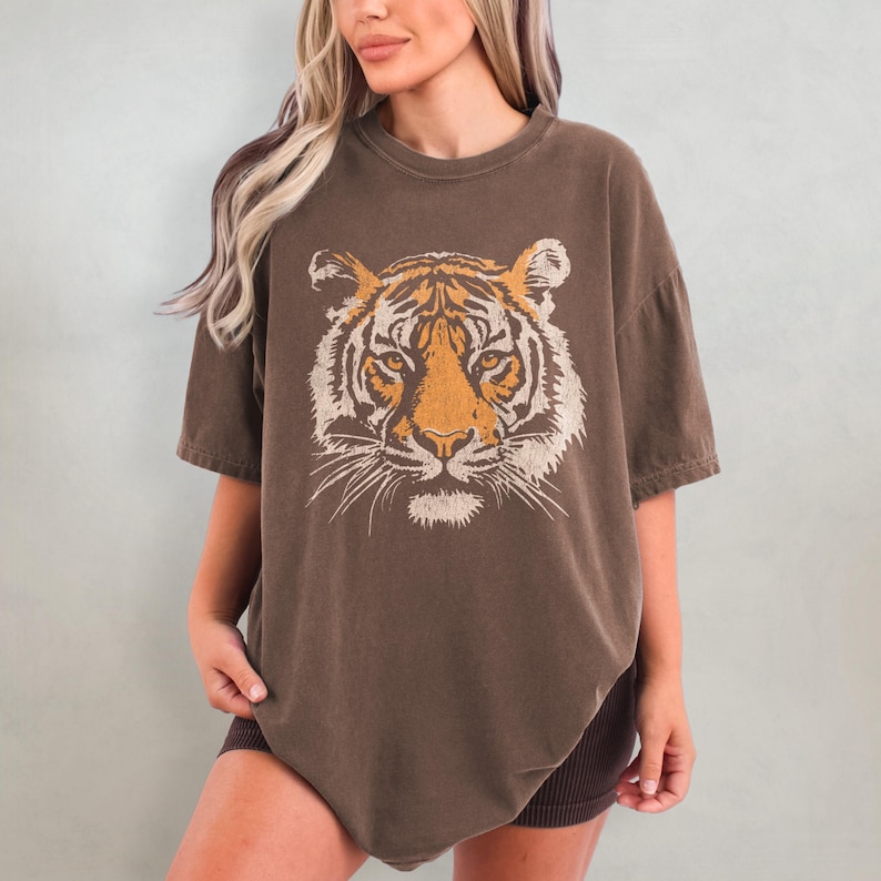 May include: A brown oversized t-shirt with a vintage-style tiger face graphic printed on the front.
