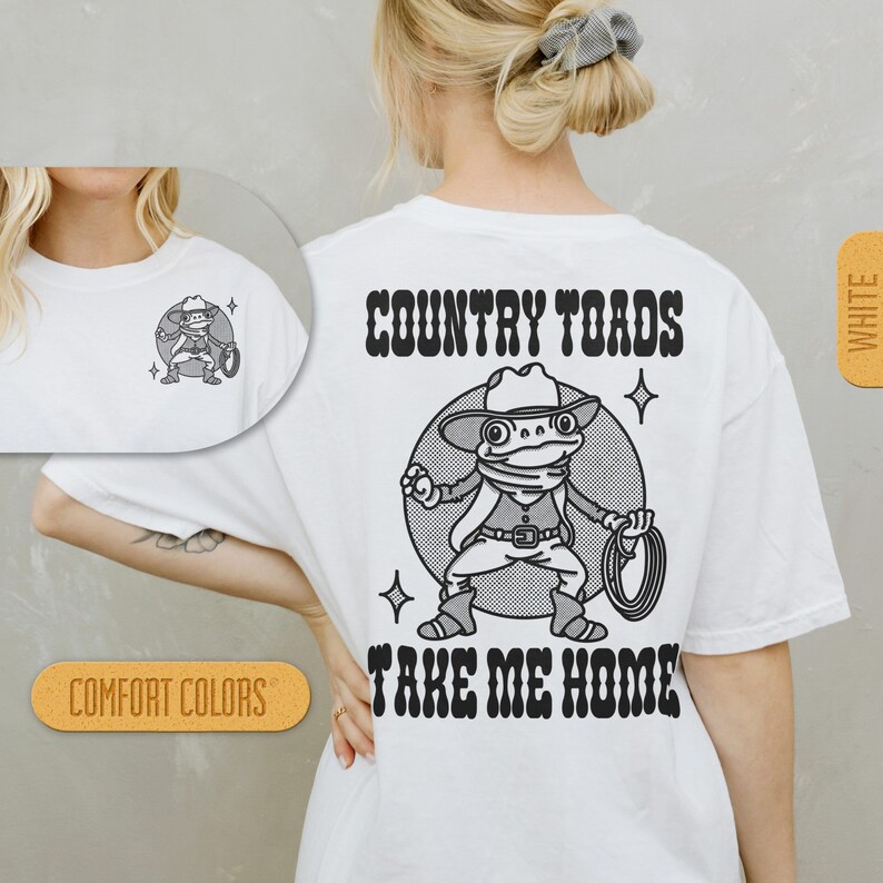 Puede incluir: Camiseta blanca con una ilustraci&oacute;n en blanco y negro de una rana con un sombrero de vaquero y sosteniendo un lazo. El texto "COUNTRY TOADS TAKE ME HOME" est&aacute; impreso en negro en la camiseta.