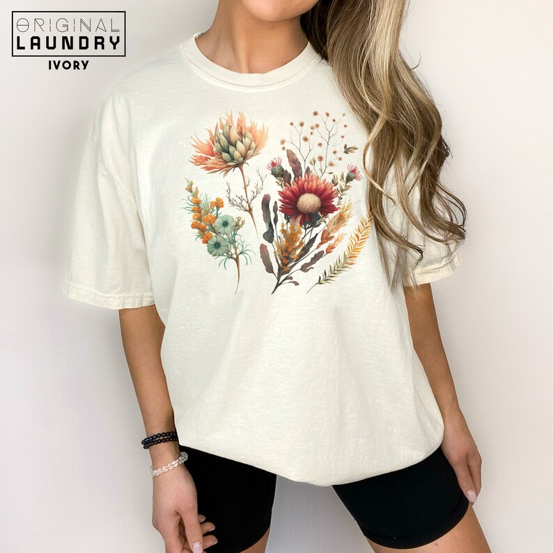 May include: A white t-shirt with a floral print featuring a variety of flowers in shades of red, orange, yellow, and green.