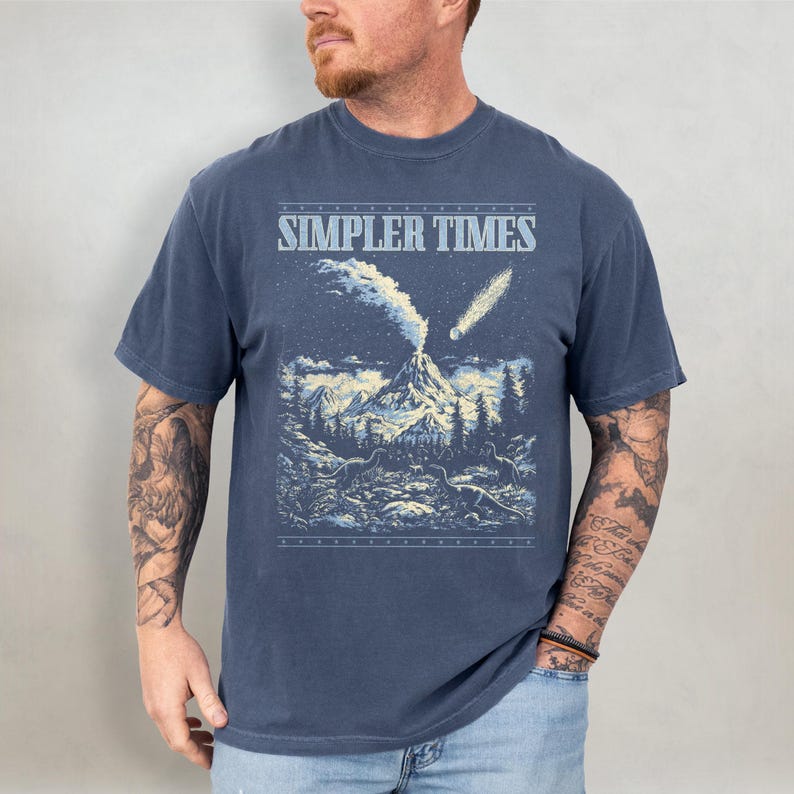 K&ouml;nnte beinhalten: Marineblaues T-Shirt mit dem Text "SIMPLER TIMES" &uuml;ber einer Berglandschaft mit Vulkan, B&auml;umen und Kometen. Die Grafik ist in Blau- und Wei&szlig;t&ouml;nen gehalten.