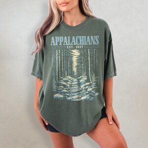 May include: A dark green oversized t-shirt with a vintage-style graphic print of a forest path. The print features the text "Appalachians Est. 1937".