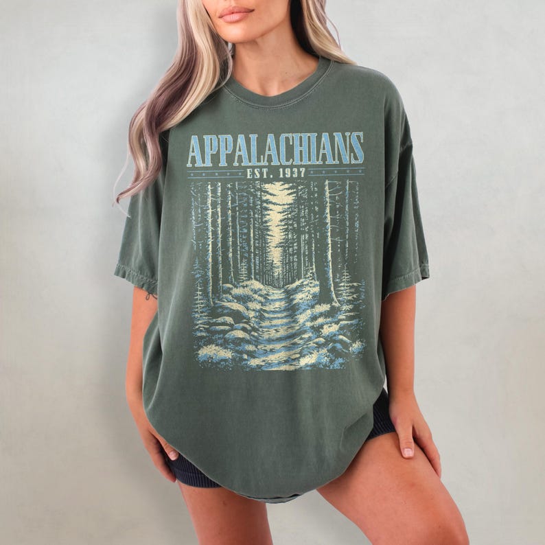 May include: A dark green oversized t-shirt with a vintage-style graphic print of a forest path. The print features the text "Appalachians Est. 1937".