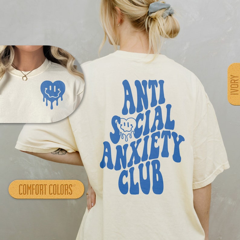 K&ouml;nnte beinhalten: Ein wei&szlig;es T-Shirt mit blauem Text, der "Anti Social Anxiety Club" in einer Retro-Schriftart lautet. Die R&uuml;ckseite des Shirts zeigt ein blaues, tropfendes Smiley-Gesichtsherz.