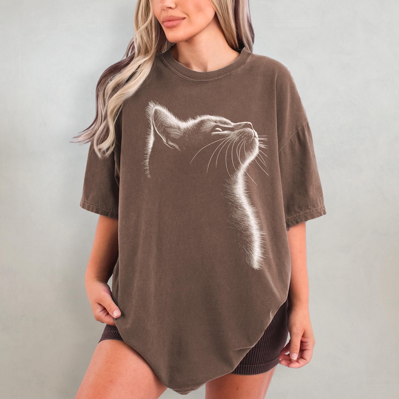 May include: An oversized brown t-shirt featuring a white outline of a cat's face looking upwards.