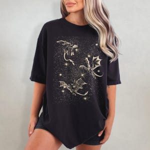 May include: Black oversized t-shirt with a graphic print of three gold dragons flying in a starry sky.